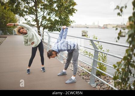 Young people doing stretching exercises during sports training in the park outdoors Stock Photo