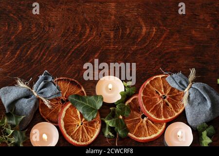 Dark brown wooden table background for text, decorated with dried orange, ivy evergreens, blue cotton bags to look festive and cozy for Yule Stock Photo