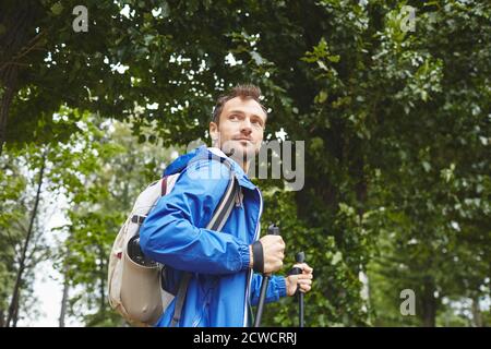 Portrait of young man with backpack behind his back using sticks for sport walking outdoors Stock Photo