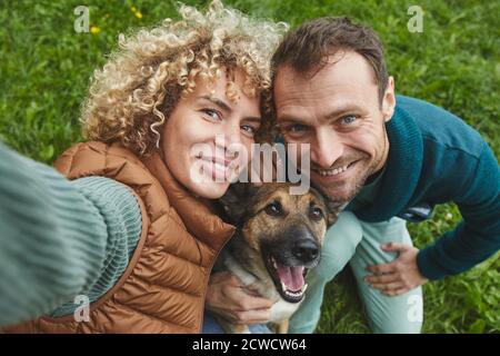 Portrait of young couple with dog smiling at camera while walking on the nature Stock Photo