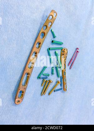 explanted titanium screws and titanium plates in different colors and sizes lie on a blue cloth Stock Photo