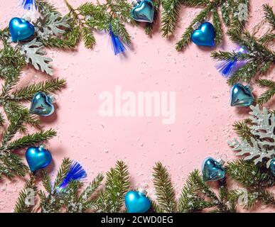 Blue heart shape Christmas ornaments with blue led party lights on pastel pink background, decorated with fir tree branches. Round border, lot of copy Stock Photo