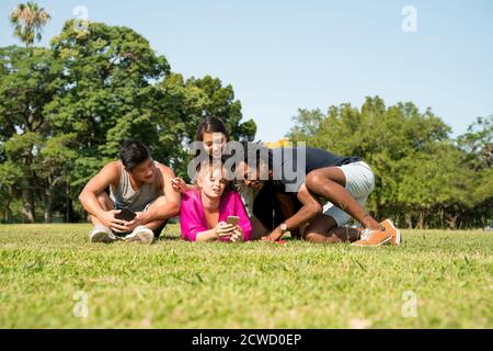 A multi-ethnic group of friends using their mobile phones while laying together in the park. Stock Photo