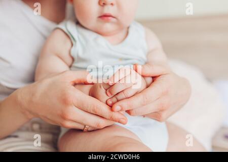 Close up of kid's hands. Woman sitting on bed with her newborn baby son hugging child. Family relaxing at home.