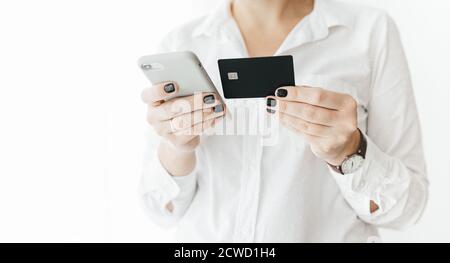 Unrecognizable woman wearing white shirt holding black credit card and smartphone, making online payment, online shopping, lifestyle technology Stock Photo