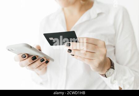 Unrecognizable woman wearing white shirt holding black credit card and smartphone, making online payment, online shopping, lifestyle technology Stock Photo