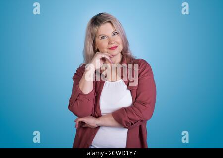 Caucasian woman posing on a blue studio wall gesturing a wonder touching her chin and look at camera Stock Photo