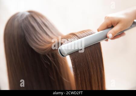 Close up hands of professional hairdresser beauty salon, straighteners curling female hair Stock Photo