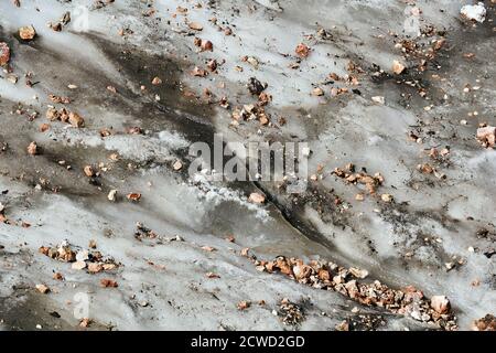 muddy surface of a melting mountain glacier covered with rocks and rubble Stock Photo