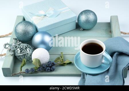 Beautiful Christmas composition with a gift box, a Cup of coffee balls and a branch with berries on a soft blue tray. Stock Photo