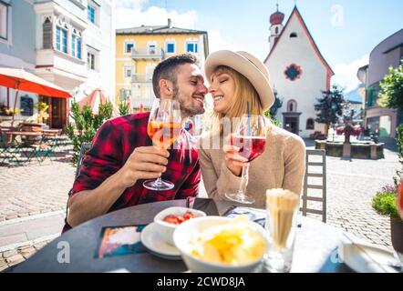 Happy couple taking an aperitif in a cafè. Man and woman on their honeymoon travel on the italian dolomites. Visiting a traditional village in a mount Stock Photo