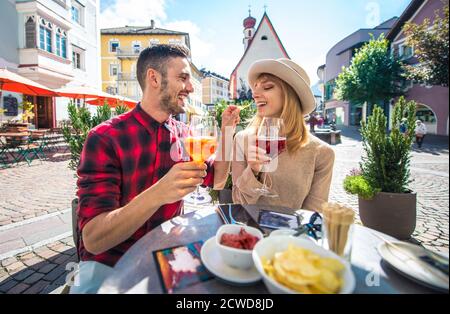 Happy couple taking an aperitif in a cafè. Man and woman on their honeymoon travel on the italian dolomites. Visiting a traditional village in a mount Stock Photo
