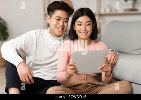 Japanese Spouses Using Tablet Watching Movie Online Relaxing At Home Stock Photo