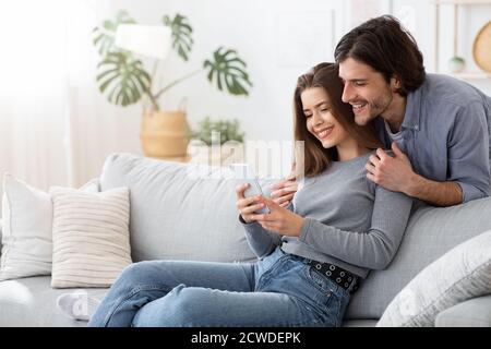 Positive young couple using mobile phone at home Stock Photo