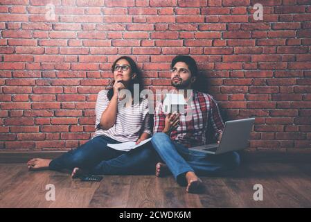 Focused Indian young couple accounting, calculating bills, discussing planning budget together using online banking services and calculator, checking Stock Photo