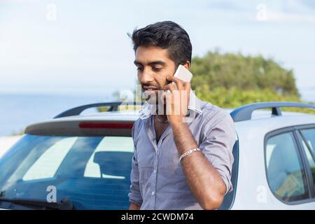 Man talking on a cell phone leaning on the door of his car having a conversation Stock Photo