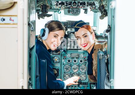 Back view from the inside of the plane. Portrait of two attractive young women pilots with headset preparing to fly. Happy pilots. Couple in aviation Stock Photo