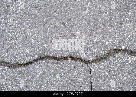 An area paved with asphalt is seen from above with a large crack running through it, and another smaller perpendicular crack below. Stock Photo