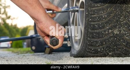 Man changing wheel. tire changer changing flat car tire. Help on road concept. Mechanic hands unscrews a flat tire of a car raised on a jack Stock Photo