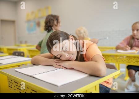 Dark-haired girl in orange tshirt sleeping on the desk Stock Photo