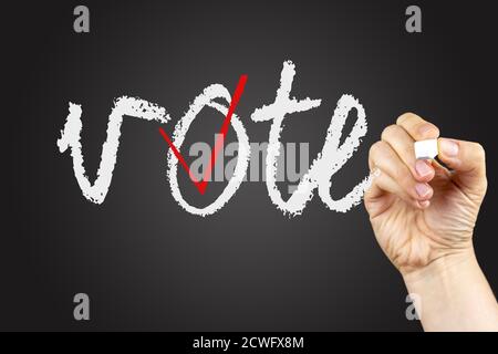 Vote phrase and checkbox on a blackboard, written with white chalk in a hand. Stock Photo