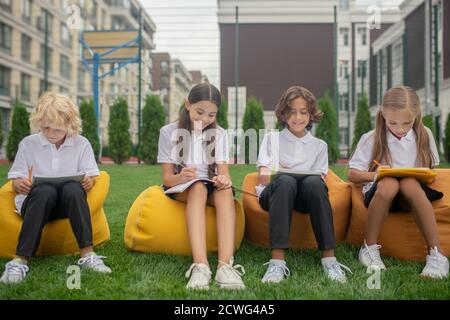 Children sitting on bag chairs and making notes Stock Photo