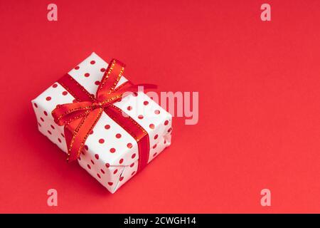 White gift wrapped in gift paper polka with festive ribbon on red background with copy space. Stock Photo