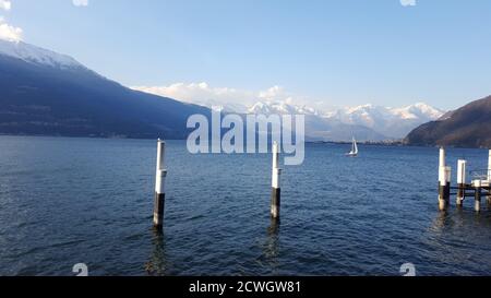 winter panoramic view of Lake Como  mountains and one boat sailing on water  from the quay in Bellano and two seagulls on two poles in foreground Stock Photo