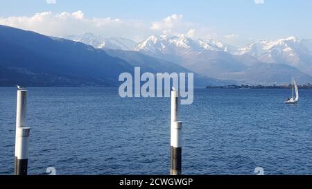 winter panoramic view of Lake Como  mountains and one boat sailing on water  from the quay in Bellano and two seagulls on two poles in foreground Stock Photo