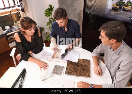 Three young architects discussing together inside a conference room the new interior design concept for a brand presentation. Young entrepreneurs work Stock Photo