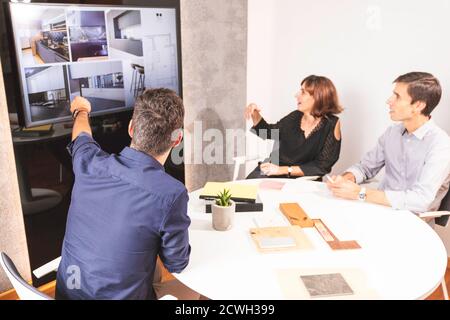 Three young architects discussing together inside a conference room the new interior design concept for a brand presentation. Young entrepreneurs work Stock Photo