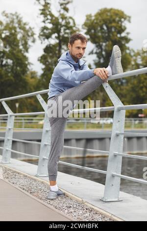 Young athlete in sports clothing standing on the bridge and doing stretching exercises during sports training Stock Photo
