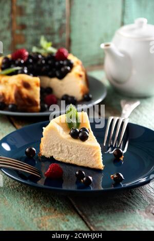 Berry cheesecake cut on deep blue plate with teaware on old painted wood background Stock Photo