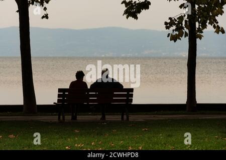 A couple of old men look at the landscape sitting on a bench at dusk Stock Photo