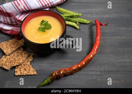 A Cup of soup-mashed peas and beans and pods of hot pepper, peas and beans on a dark wooden background with crackers from cereals. Place for a copy sp Stock Photo