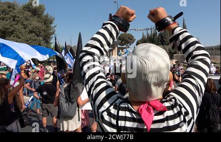 JERUSALEM, ISRAEL - SEPTEMBER 29: A protester wearing a prison uniform raises his shackled hands in front of the Israeli parliament during a demonstration over legislation restricting protests amid a nationwide lockdown aimed at curbing the coronavirus pandemic on September 29, 2020 in Jerusalem, Israel. The Israeli parliament approved changes to the Coronavirus Law that would limit protests against Prime Minister Benjamin Netanyahu demanding his resignation over his indictment on corruption charges and handling of the coronavirus pandemic. Stock Photo