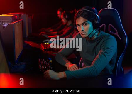 Portrait of young man looking at camera while sitting on chair in front of computer and playing game Stock Photo