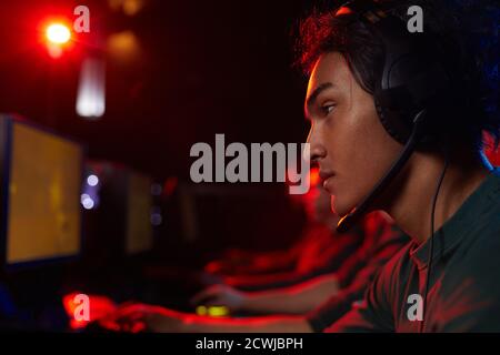Side view of young gamer wearing headphones playing computer games with his friends Stock Photo