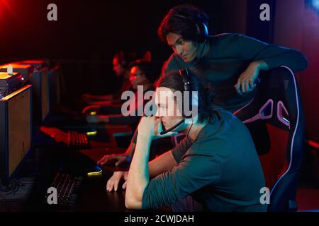 Group of friends in headphones playing computer games together in computer club Stock Photo