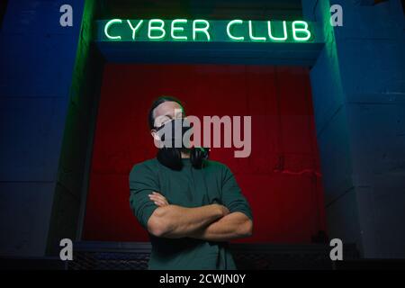 Portrait of young gamer in protective mask standing with arms crossed and looking at camera near the computer club Stock Photo