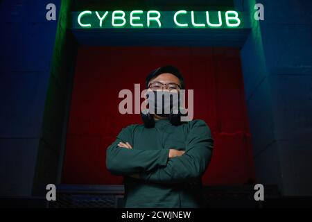 Portrait of Asian young programmer in mask standing with his arms crossed near the computer club and looking at camera Stock Photo