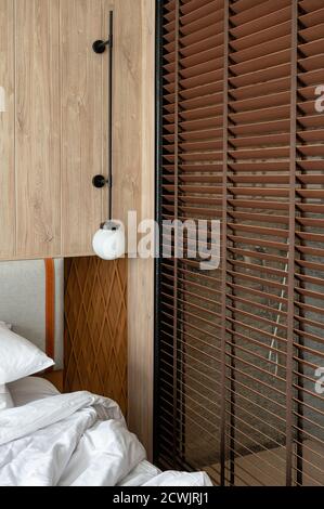 Wooden headboard with lamp and blinds in bedroom attached to bathroom Stock Photo