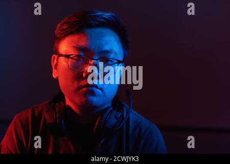 Portrait of Asian young hacker in eyeglasses and in headphones doing his criminal work in dark room Stock Photo
