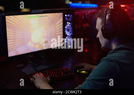 Rear view of young gamer in headphones sitting in front of computer monitor and streaming the computer game Stock Photo