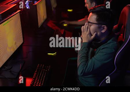 Asian young man sitting at the table in front of computer monitor he tired of playing computer games with his friends Stock Photo