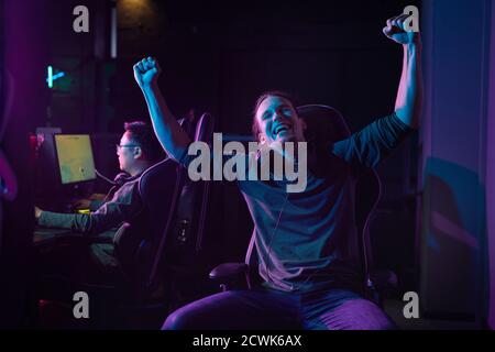 Portrait of an excited gamer sitting on a chair and enjoying his victory in a computer game Stock Photo