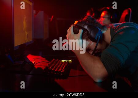 Young gamer in headphones holding his head he losing the game while sitting at the table in front of the computer Stock Photo