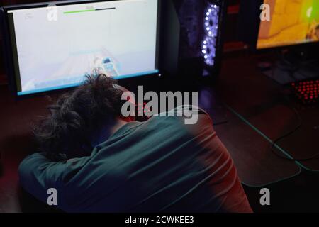Rear view of exhausted computer programmer sleeping at his workplace in front of computer monitor in dark office Stock Photo