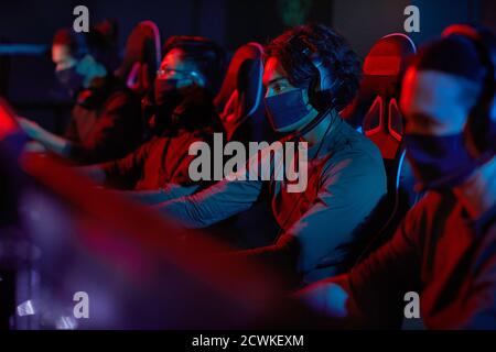Group of developers in protective masks sitting in front of computers and working in dark office Stock Photo