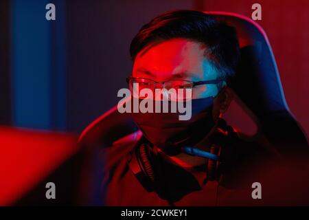 Asian programmer in eyeglasses and in protective mask concentrating on his work on computer Stock Photo